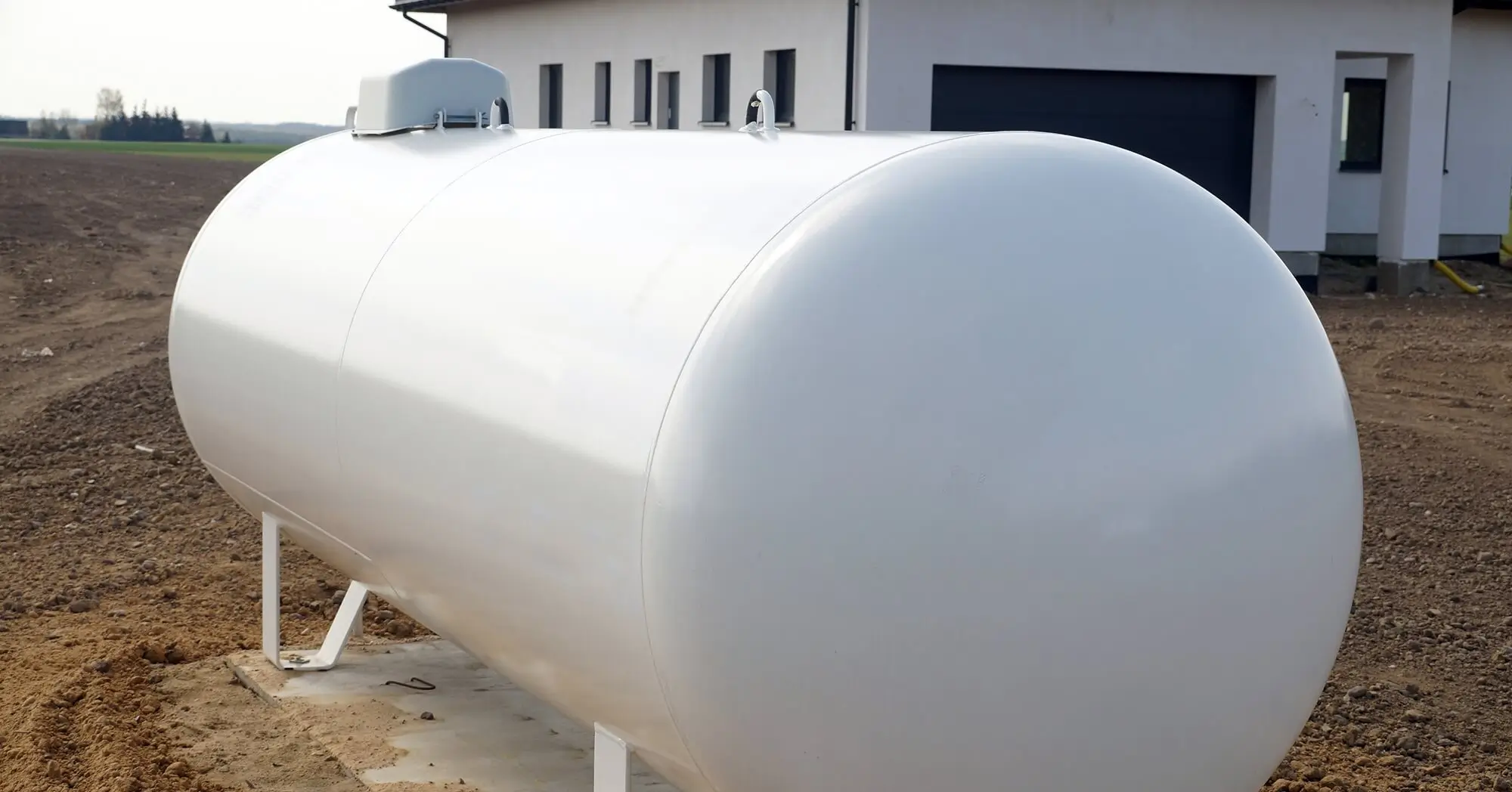 White residential LPG storage tank installed outdoors near a house.